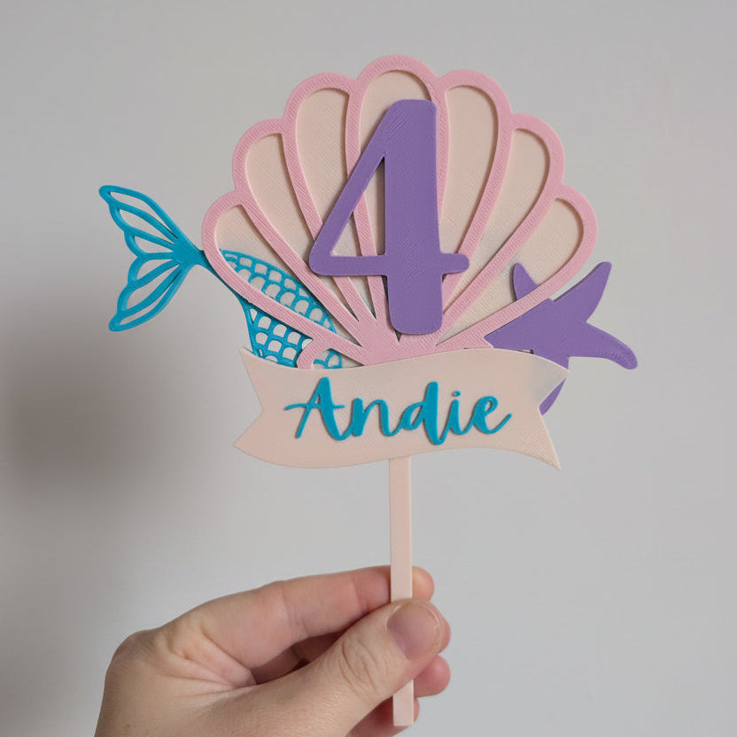 Colorful shell-shaped birthday number 4 with name 'Andie' on a stick against a plain background