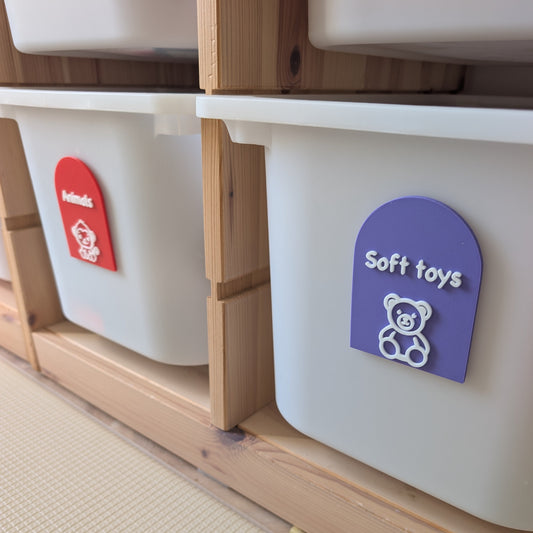 White storage bins with colorful labels on a wooden shelf.
