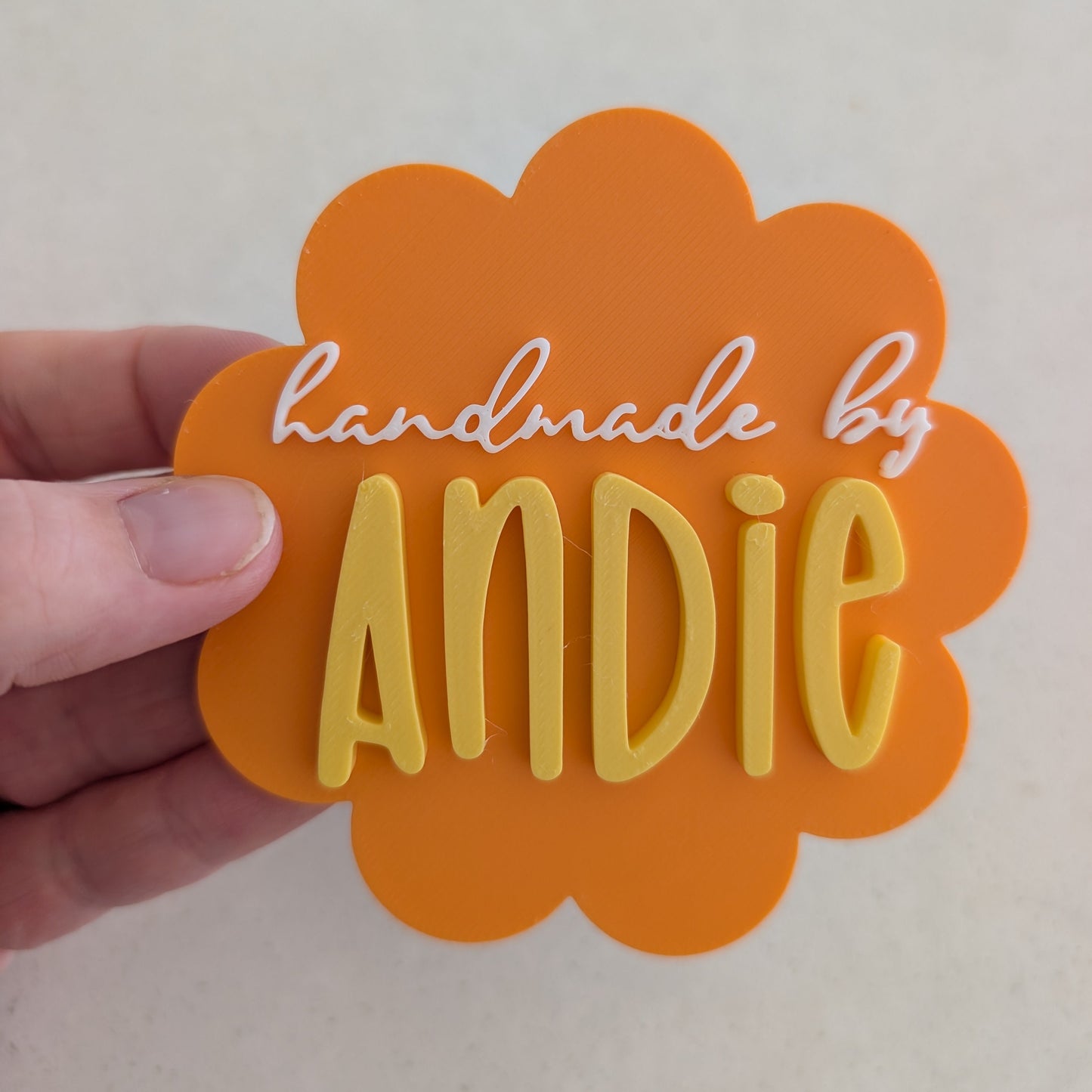 Orange cloud-shaped magnet with 'handmade by Andie' text held by a hand on a light background