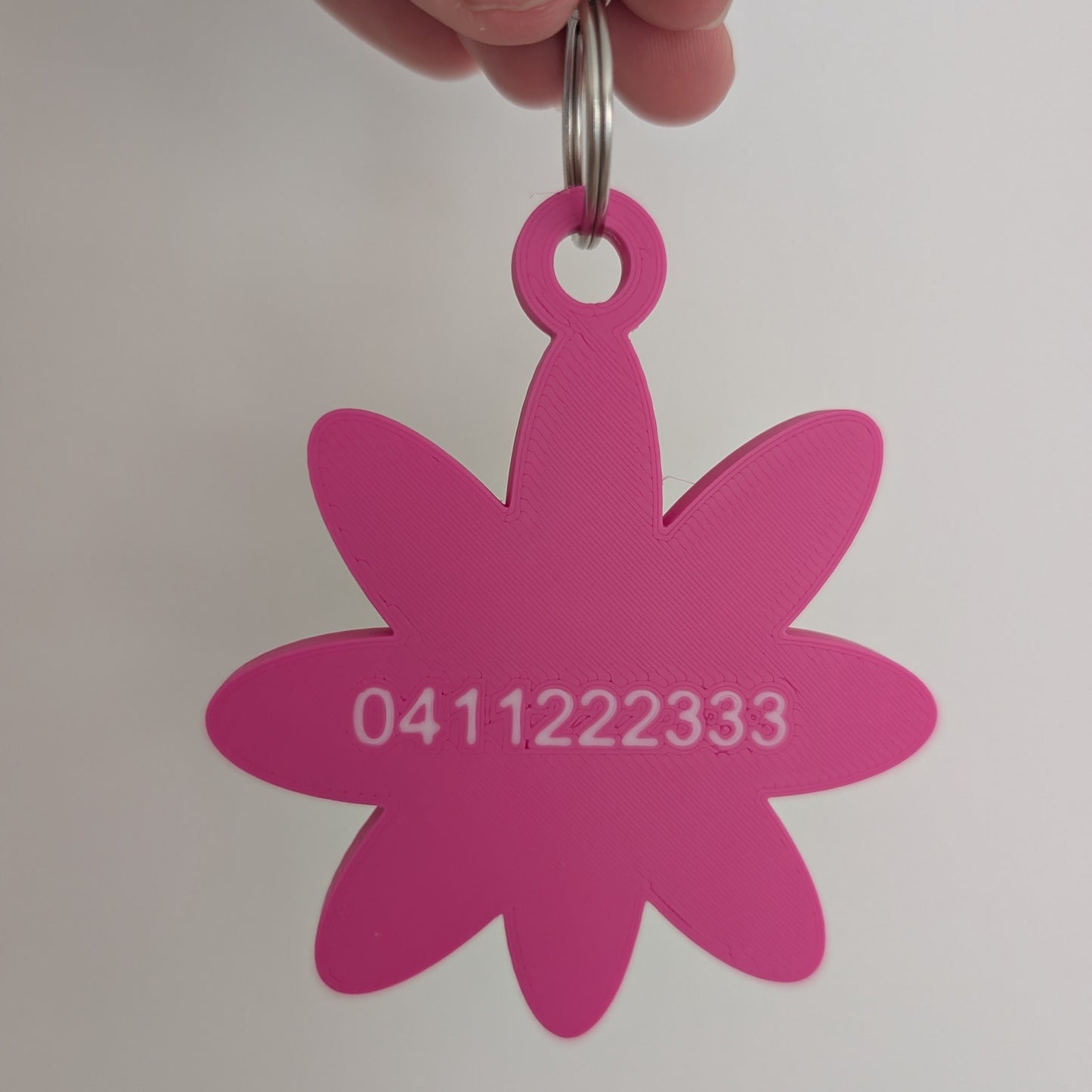 Pink flower-shaped keychain with a phone number on a white background