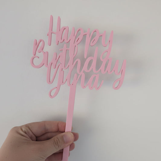 Pink 'Happy Birthday Yuna' cake topper held by a hand against a light background