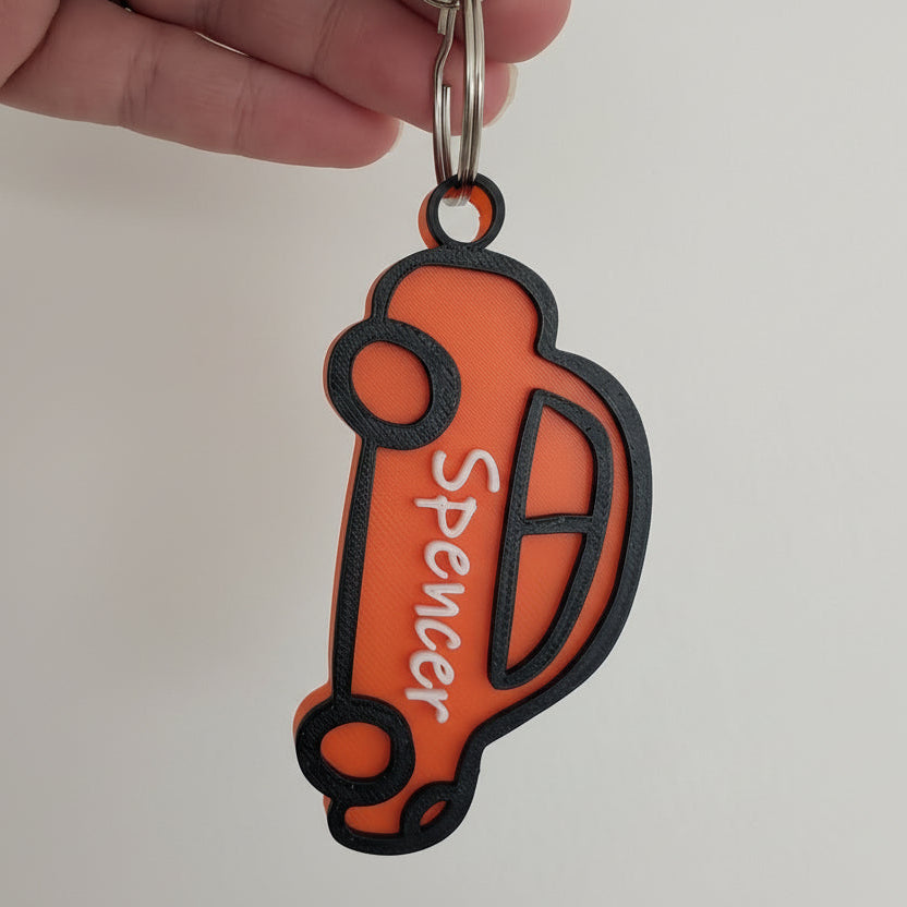 Orange and black keychain with 'Spencer' branding held by a hand against a light gray background