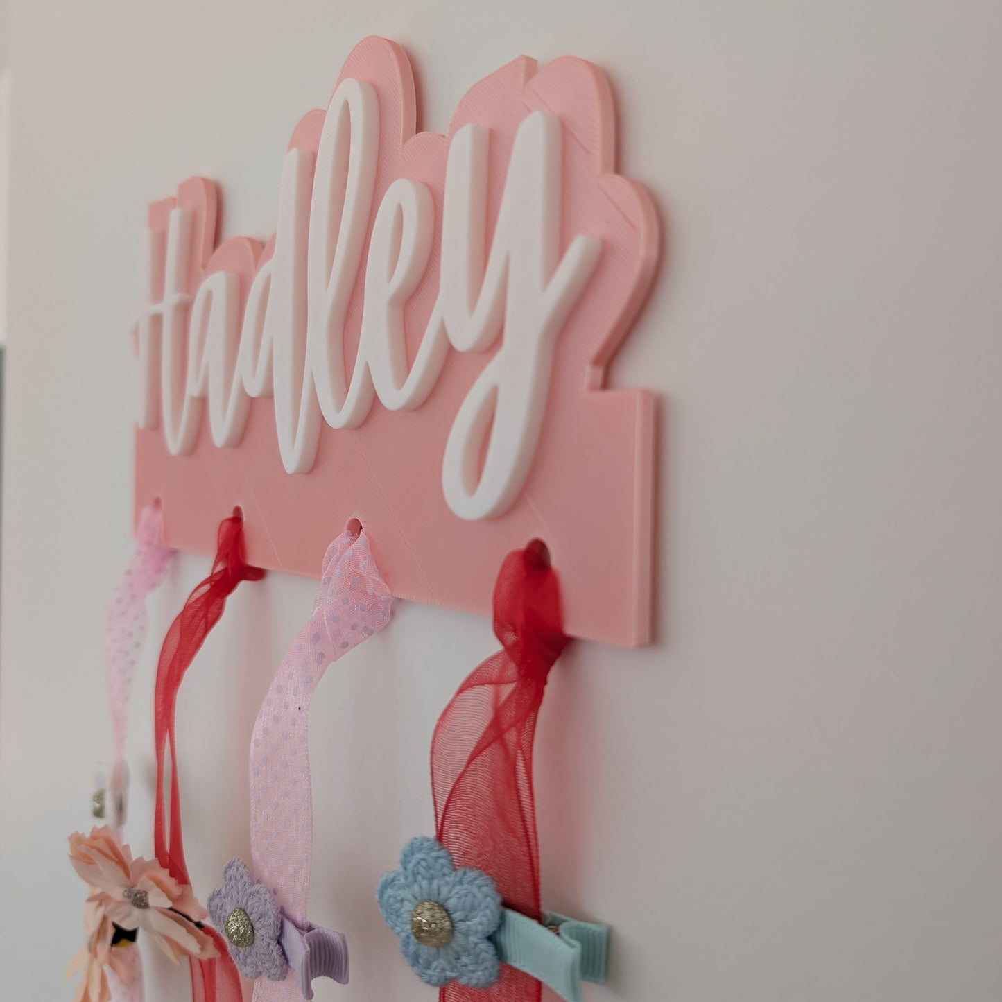 Pink decorative wall hanging with the name 'Hadley' and ribbons attached.
