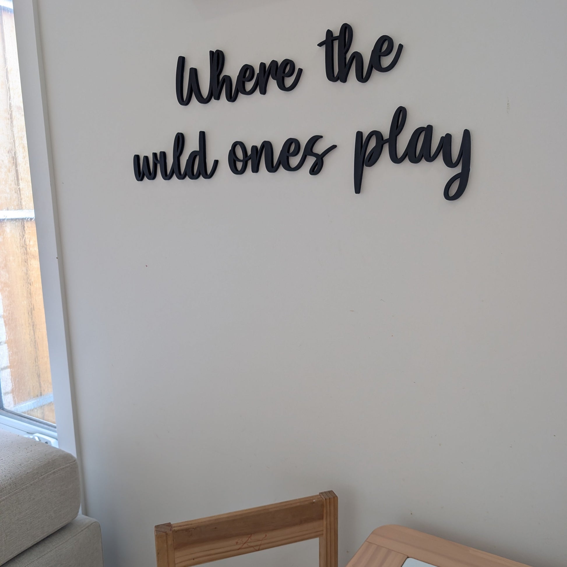 Decorative wall sign with 'Where the wild ones play' text in a room with furniture.